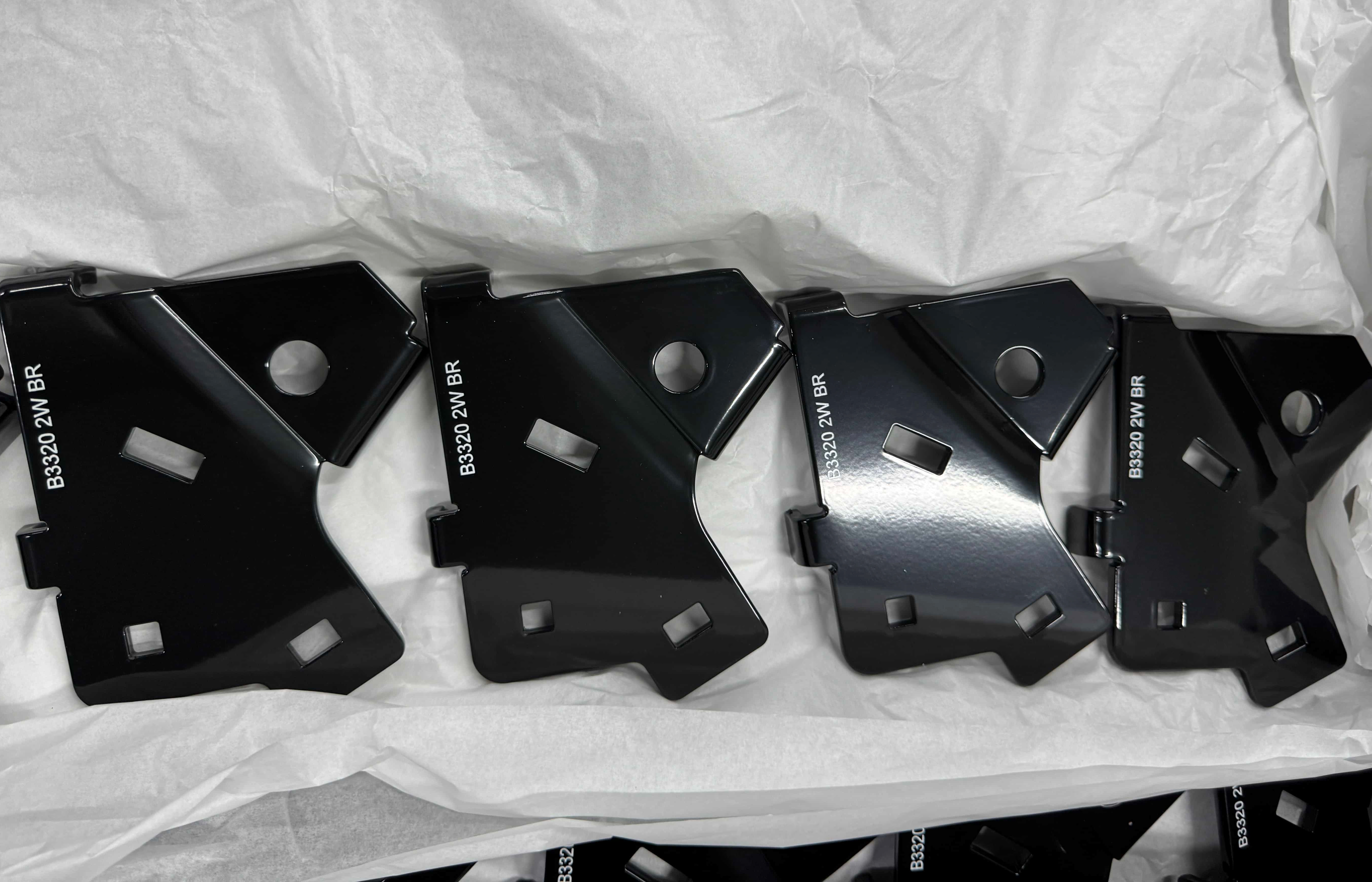 Row of black metal brackets with bent flanges and shaped cutouts.