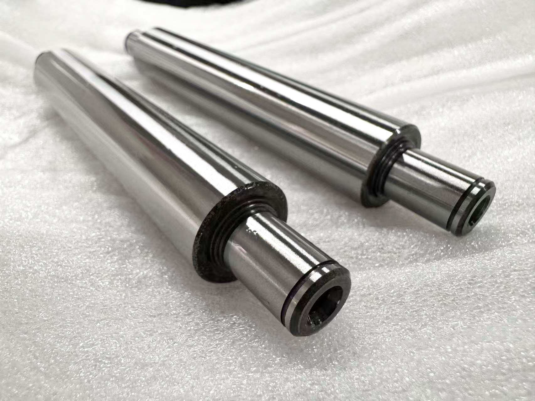 Two polished metal shafts with stepped shoulders and machined ends.