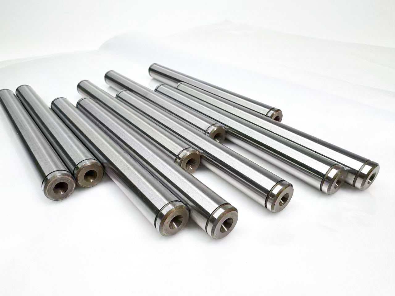 Group of polished cylindrical metal shafts with visible circular end bores.